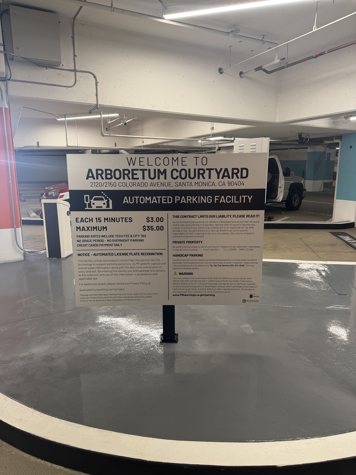 Freestanding Arboretum Courtyard parking entrance sign displaying the property name, automated parking information, rates, and terms