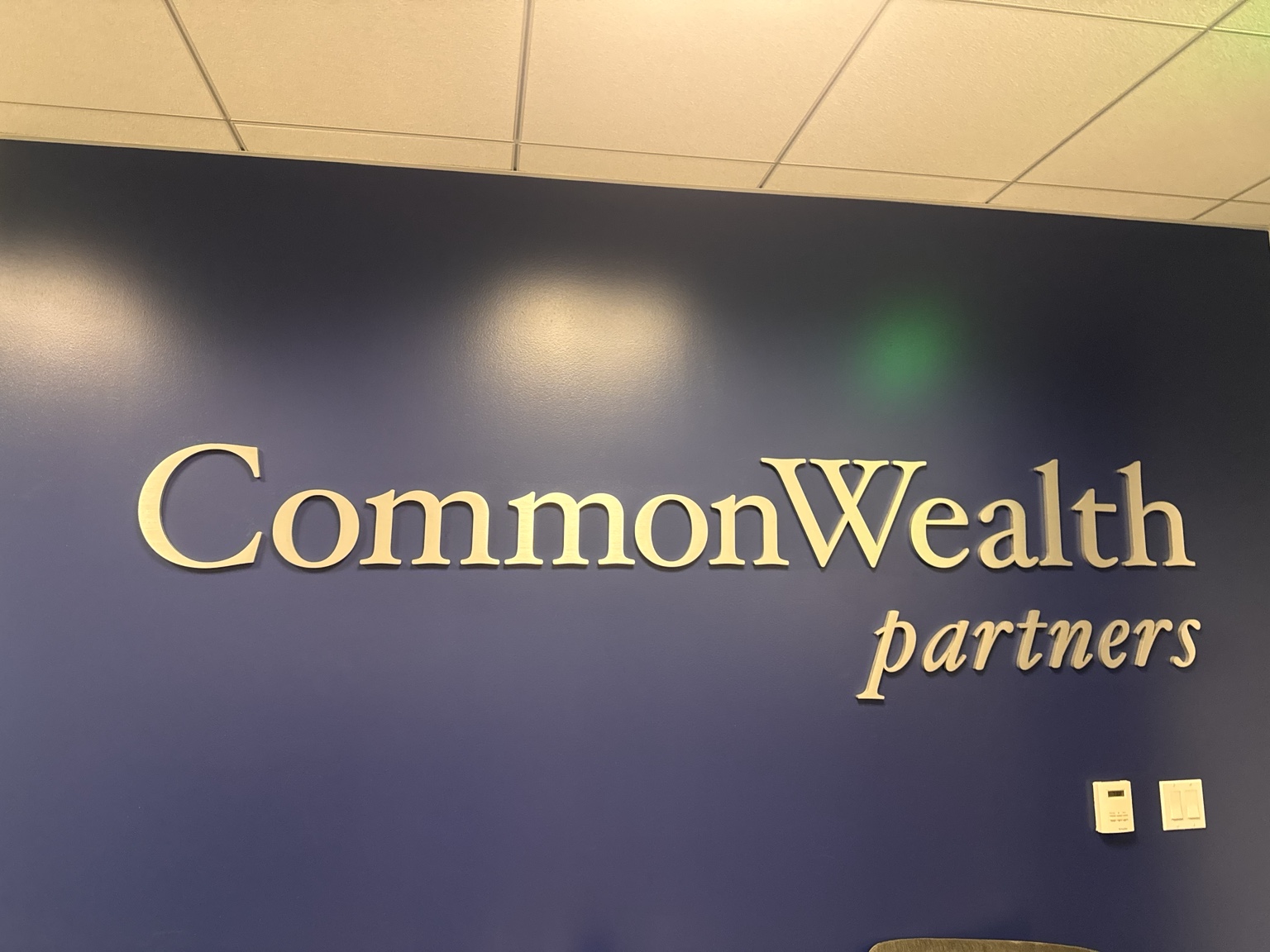 Gold-colored CommonWealth Partners metal channel letters mounted on a dark blue interior wall