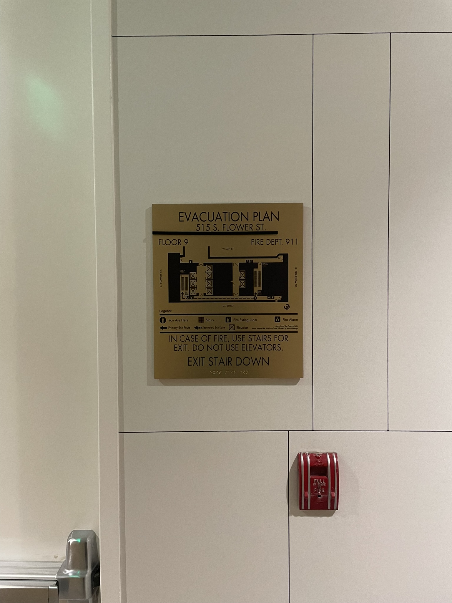 Gold-colored evacuation map for floor 9 with exit routes and Exit Stair Down lettering on a paneled wall