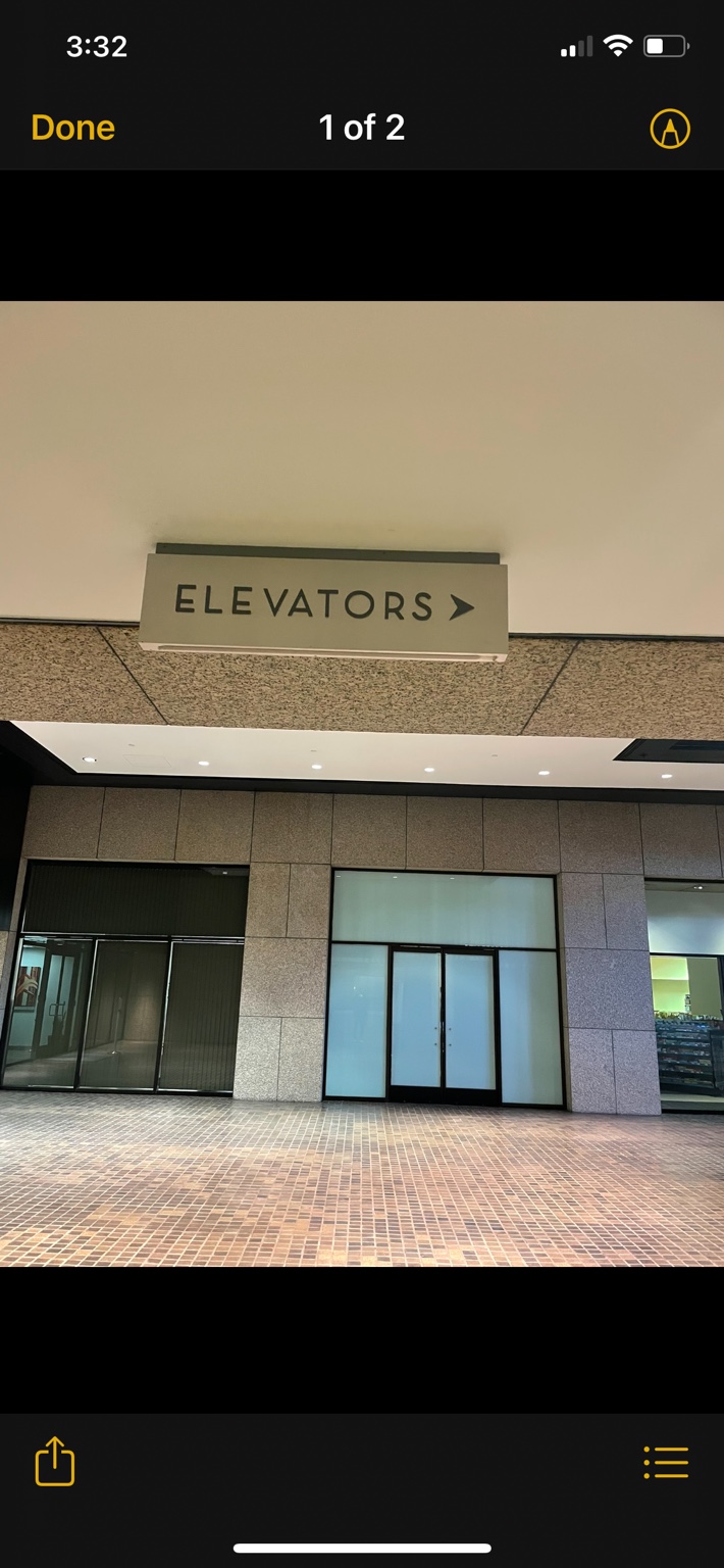 Exterior overhead sign reading Elevators with a right-pointing arrow beneath a covered walkway