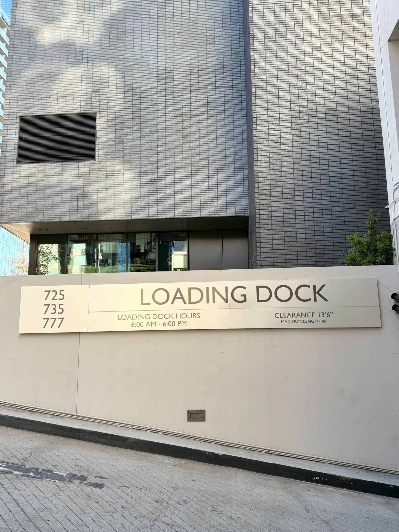 Long exterior loading dock sign displaying building numbers 725, 735, and 777, dock hours, and vehicle clearance
