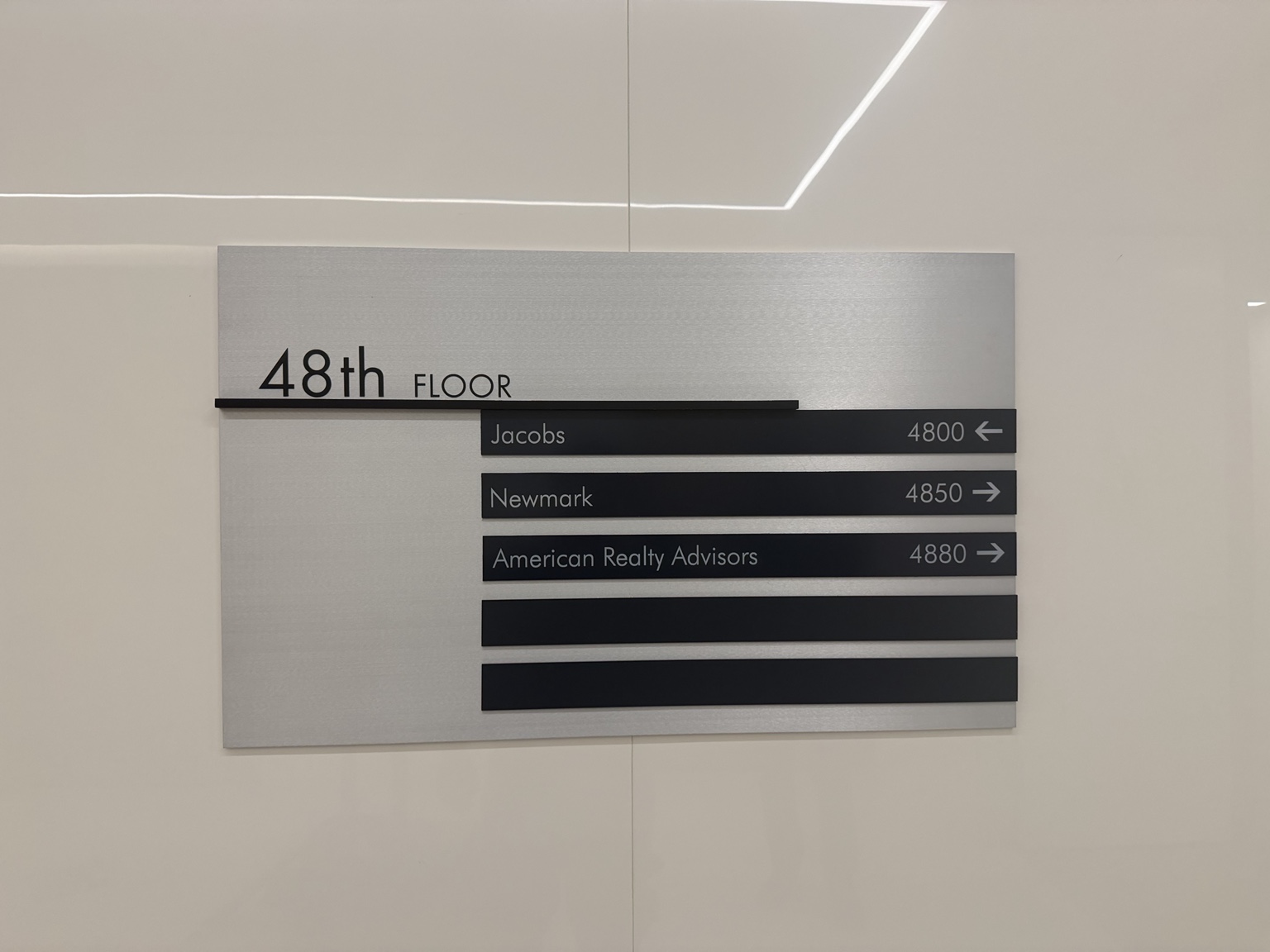 Silver 48th-floor directory with black tenant-name panels, suite numbers, and directional arrows