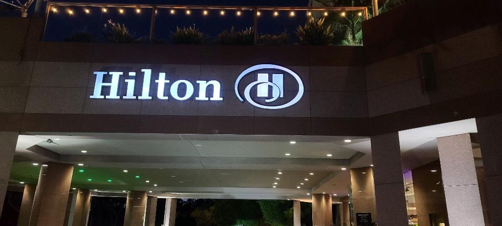 Illuminated Hilton lettering and logo above a covered exterior entrance at night