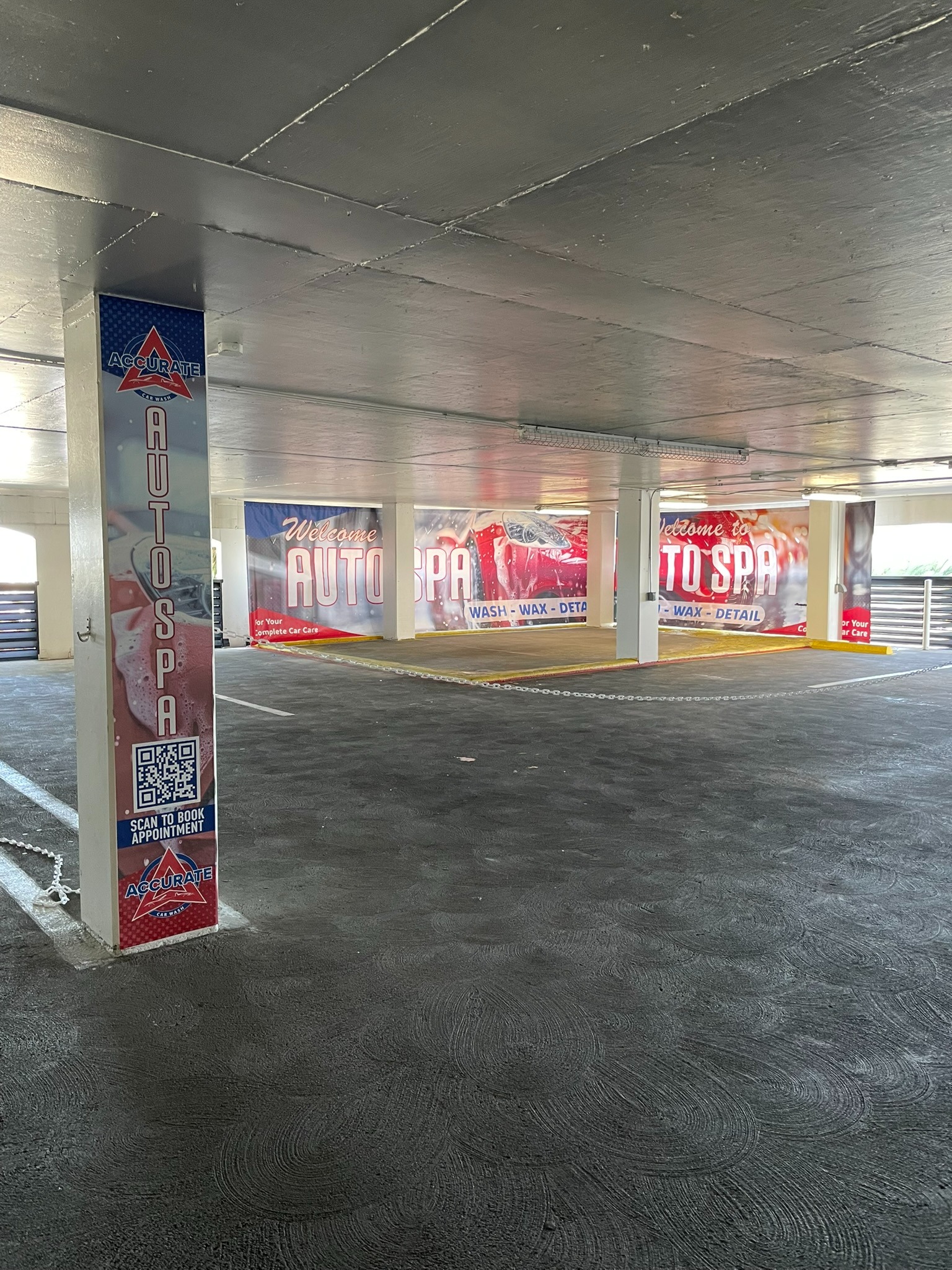 Coordinated printed wall graphics and a tall column graphic with a booking QR code in a covered parking area