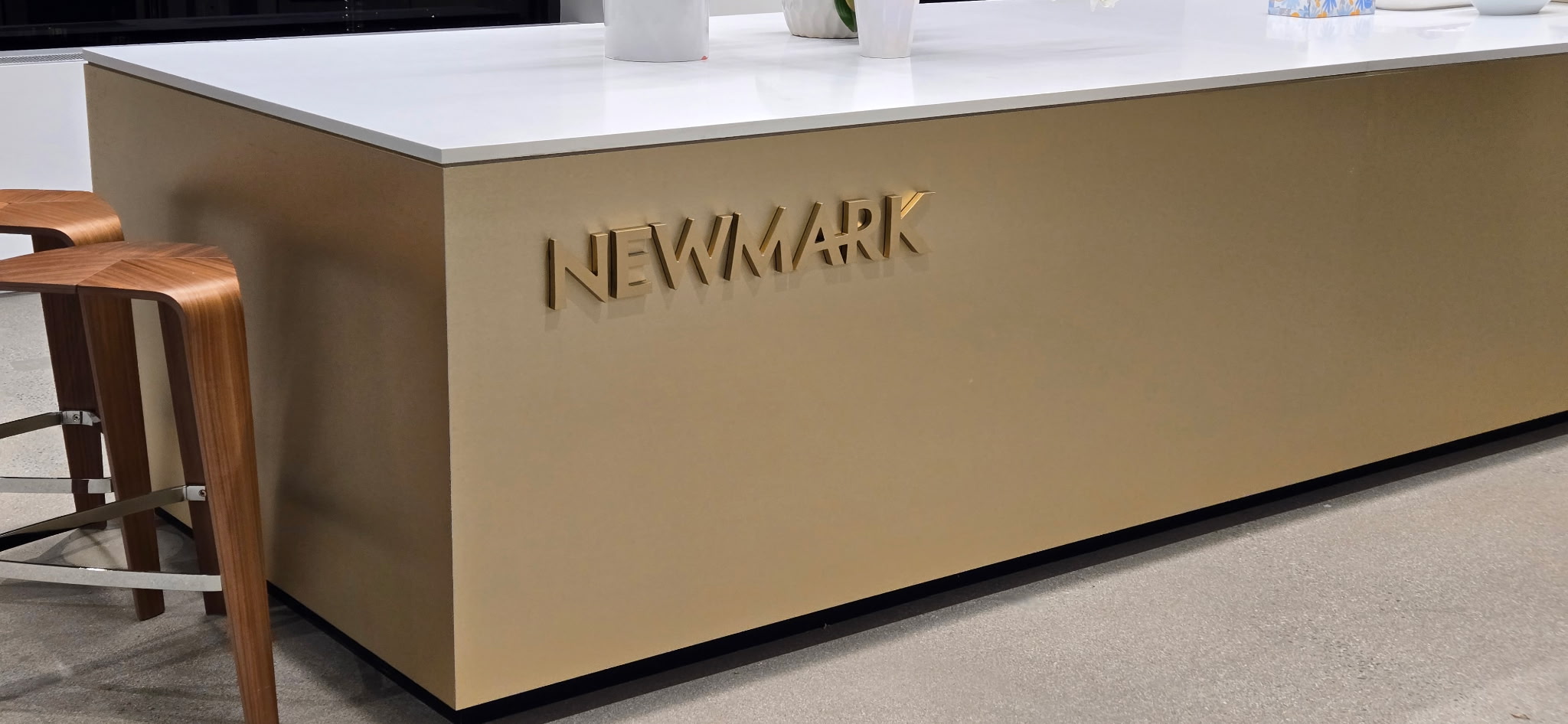 Gold-colored Newmark metal channel letters mounted on the front of an interior reception counter
