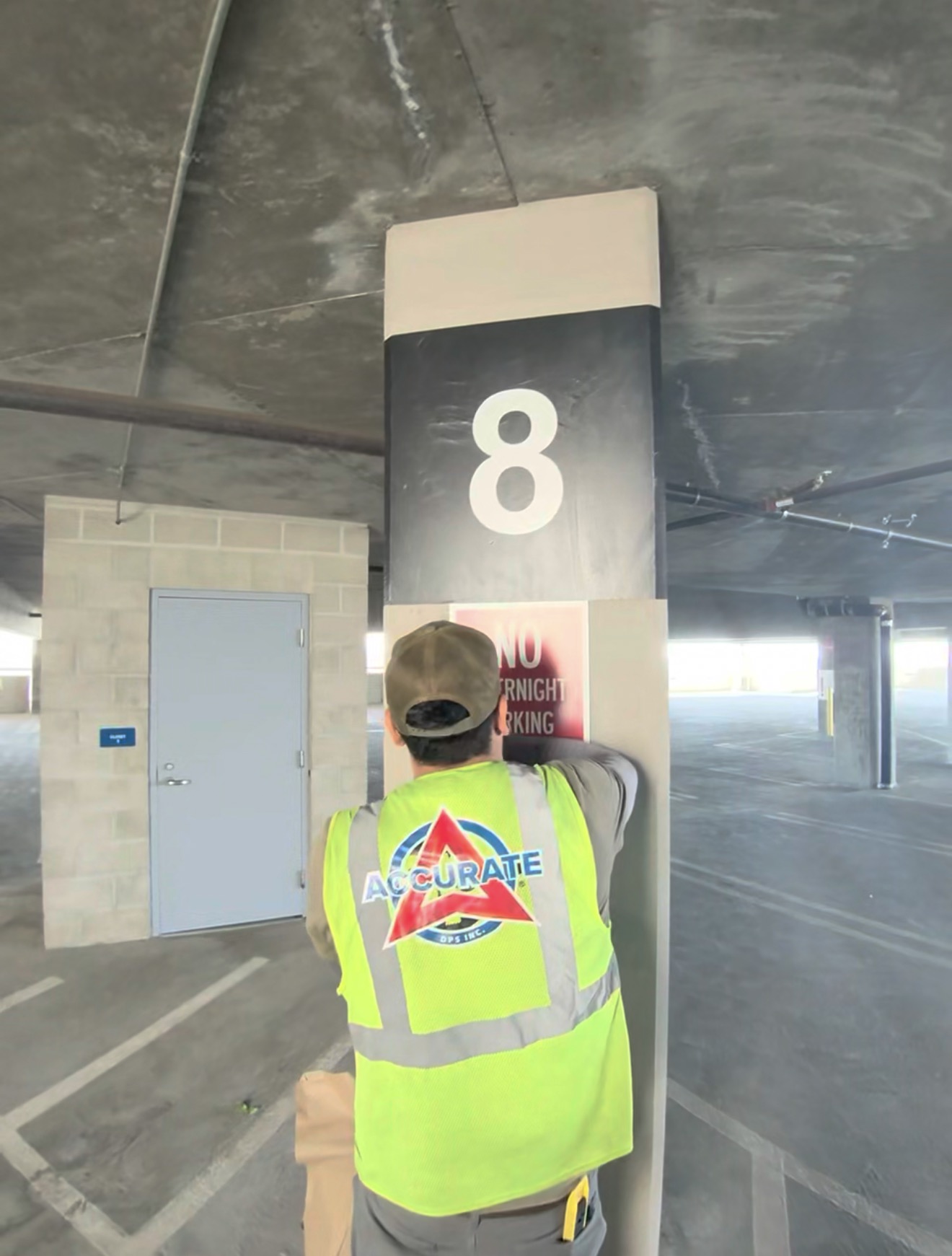 An Accurate DPS installer in a branded safety vest applying a parking sign to a garage column