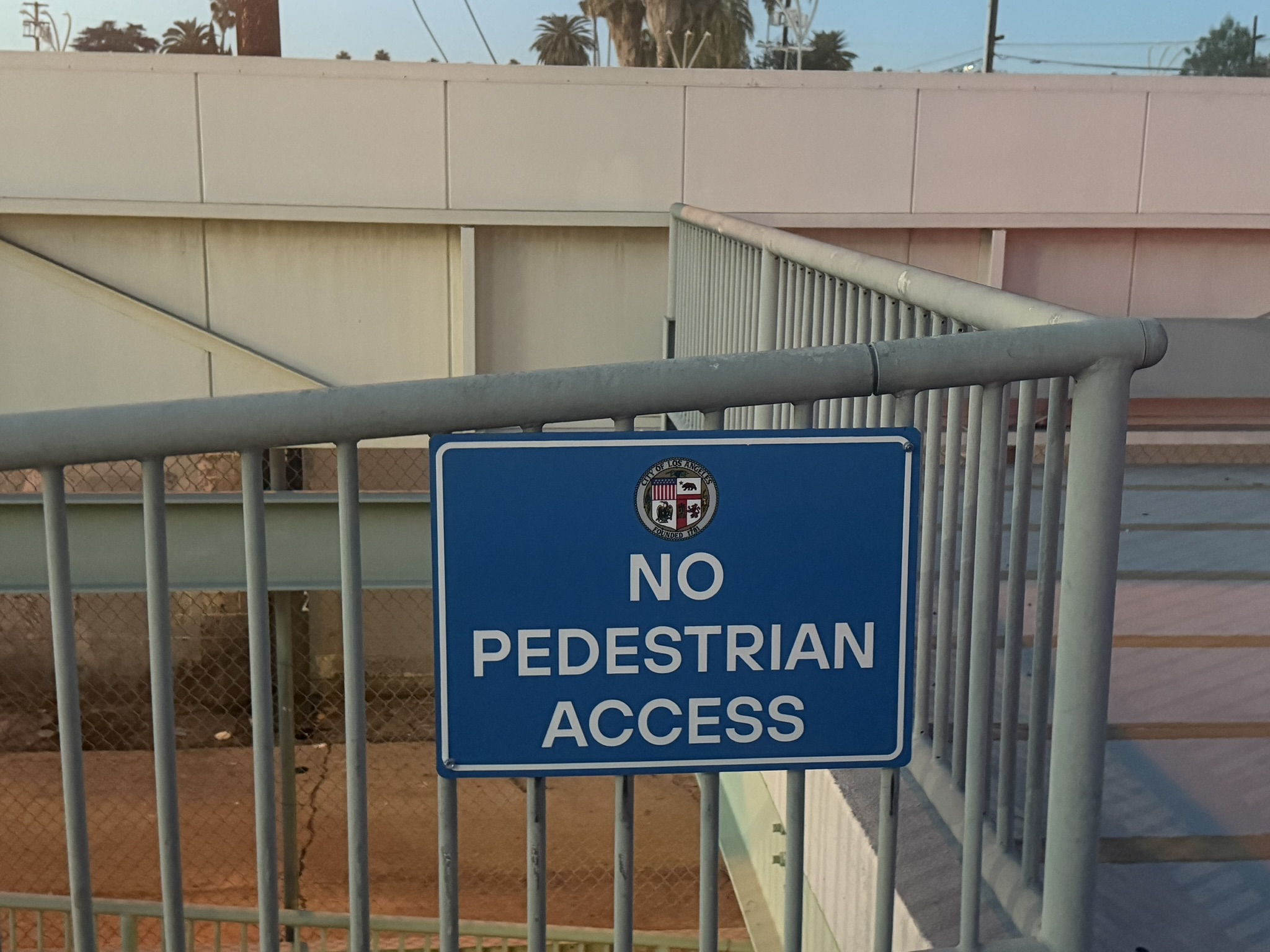 Blue No Pedestrian Access sign mounted on a metal railing beside stairs